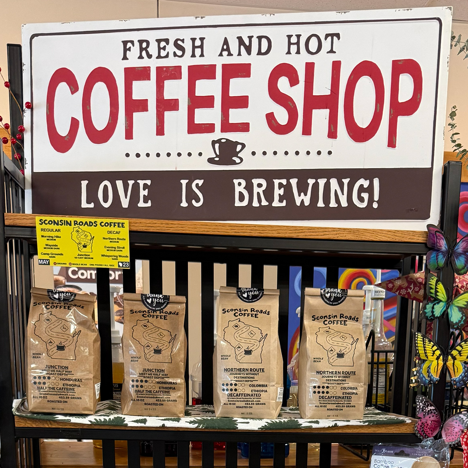 Sign "Fresh and Hot Coffee Shop Love is Brewing" with shelves of Sconsin Roads Coffee bags below